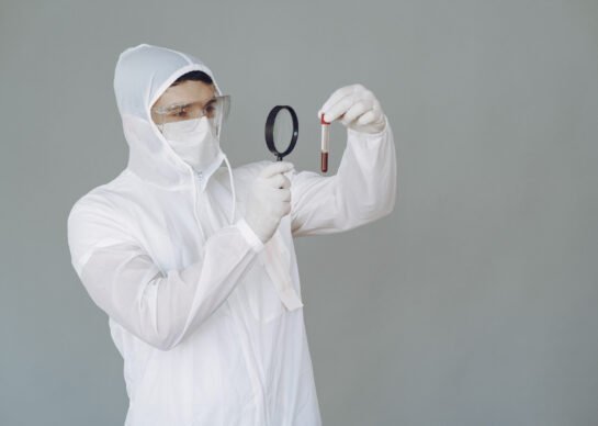 Corona virus theme. Man in a protective suit. Doctor looks at the blood tube.