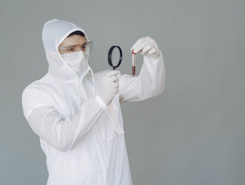 Corona virus theme. Man in a protective suit. Doctor looks at the blood tube.