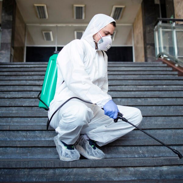 Person in white chemical protection suit disinfecting public corridors and steps to stop spreading highly contagious corona virus.