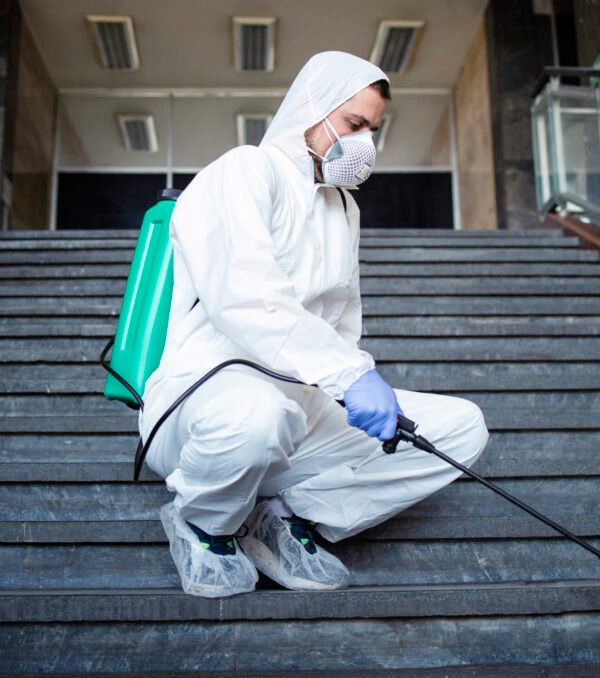 Person in white chemical protection suit disinfecting public corridors and steps to stop spreading highly contagious corona virus.