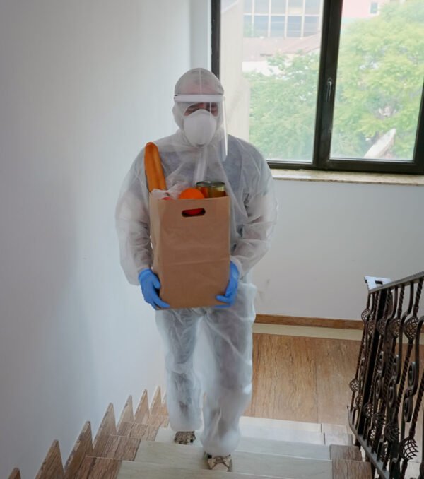 Volunteer delivering food order wearing coverall suit in covid-19 pandemic.